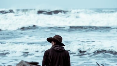 戴着棕色帽子的人站在大海前面
